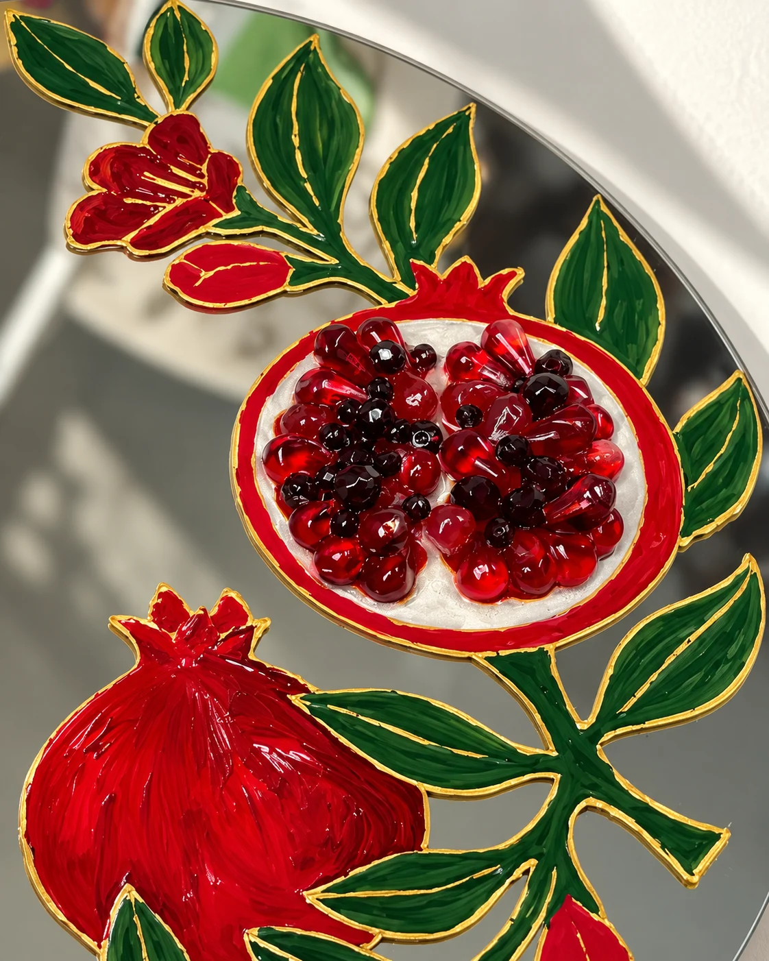 Close-up of the painted pomegranate, gold outlines and raised ruby-colored seeds