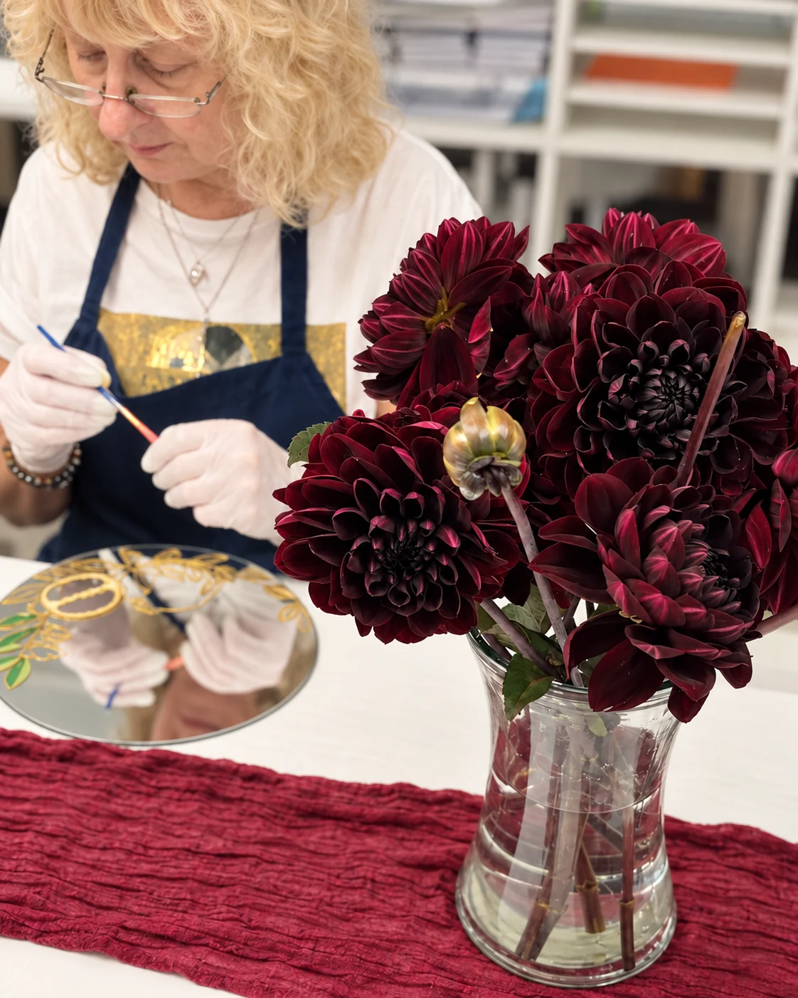 Workshop participant painting beside a vase of burgundy dahlias