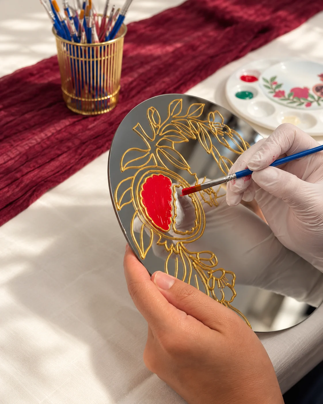 Hands painting a red pomegranate on a round mirror